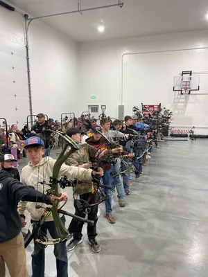 Large group of youth lined up with compound bows in the gym