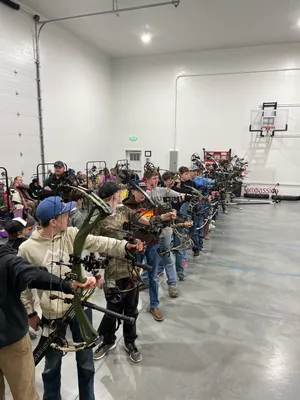 Youth lined up aiming compound bows during archery camp