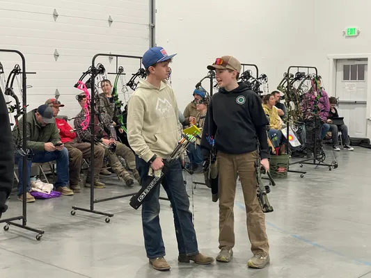 Two youth chatting between rounds with bow racks in background